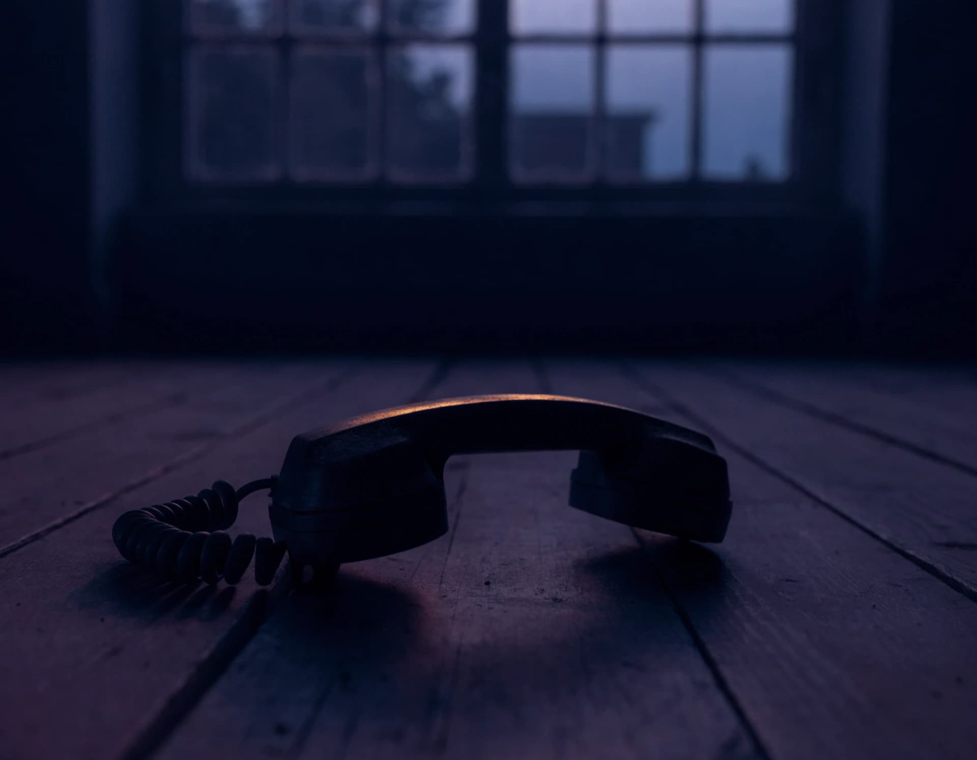 A corded telephone handset lying alone on bare floorboards in a cold, dark room, a single thin rim of warm pre-dawn light along its edge.